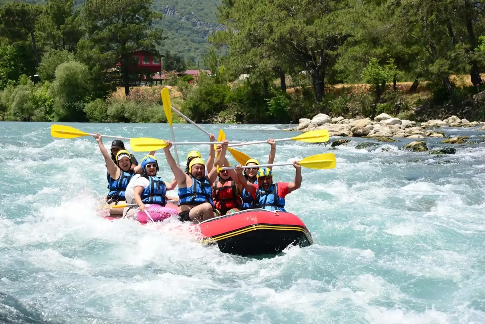 Kürekleri havaya kaldırmış neşeli rafting grubu